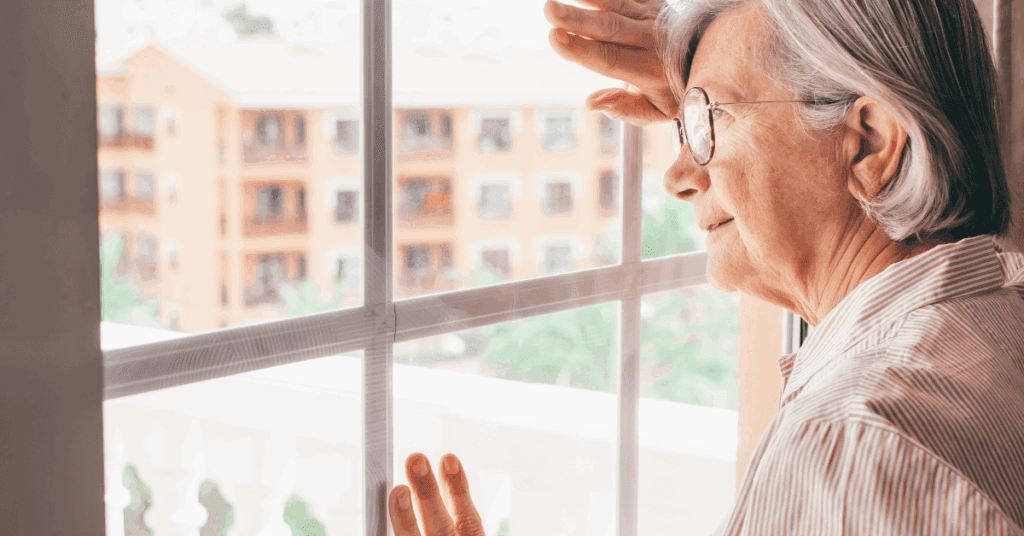 a senior woman looking out the window of her memory care residence, appearing calm