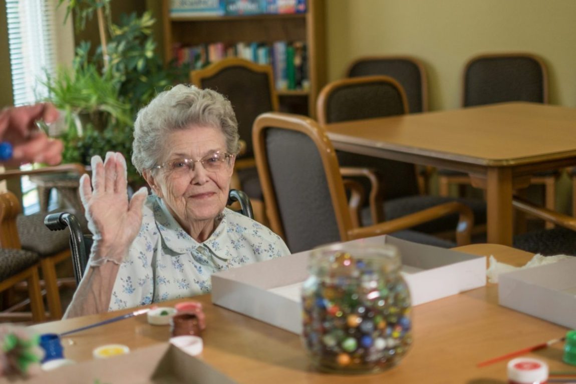 A senior woman waves during an art focused activity at Heritage Lexington.