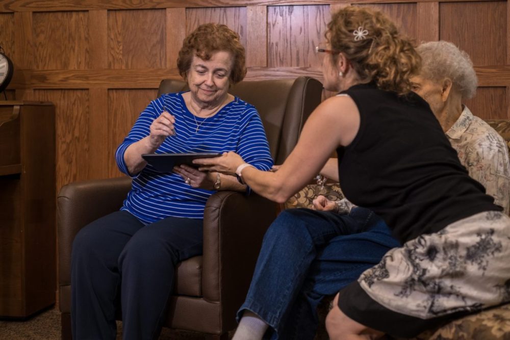 A senior woman and her friends use an iPad tablet.
