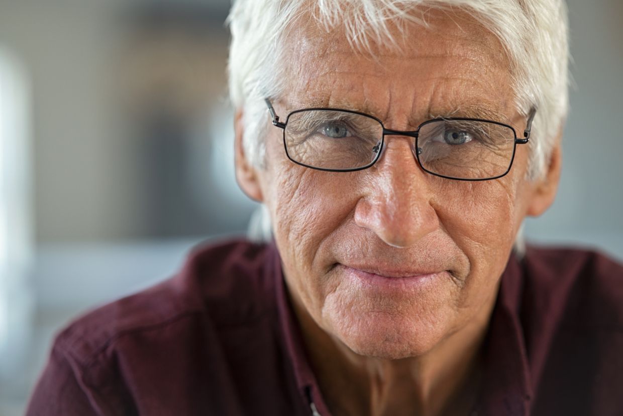 Senior man exhibiting signs of the normal aging process, including wrinkles in the skin, a need for glasses and white hair.