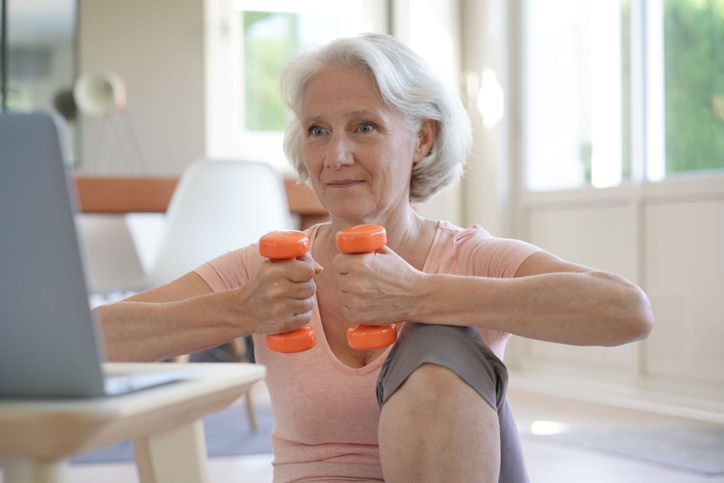 Senior woman participating in an online fitness class inside of her home.