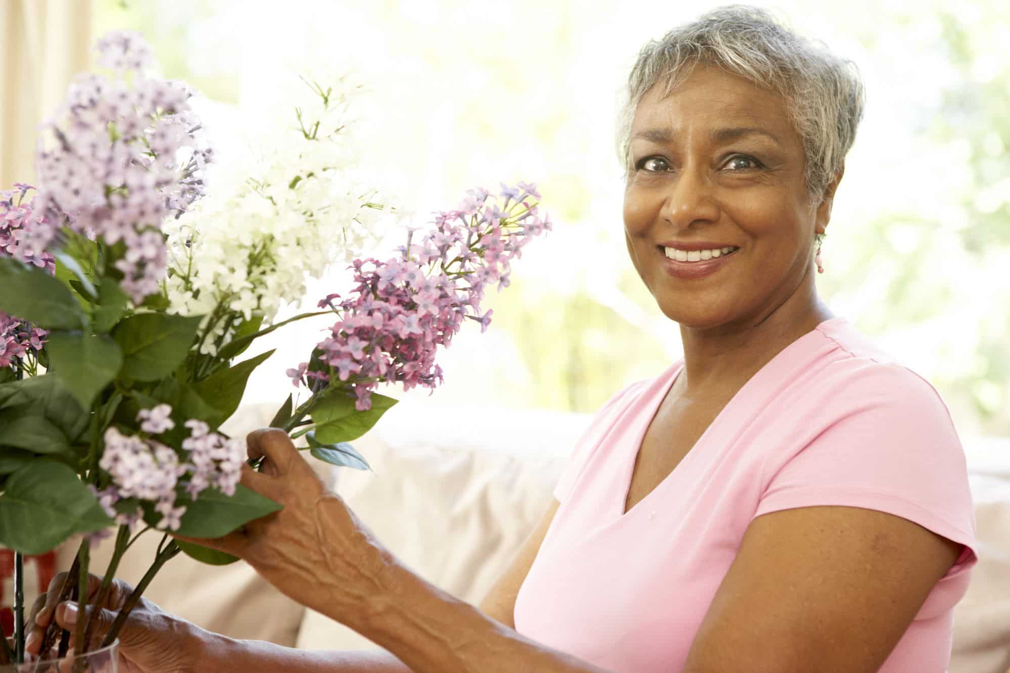 A senior woman staging her home to sell by placing floral arrangements in the living area.