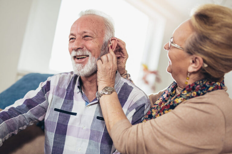 Older woman putting hearing aid in mans ear