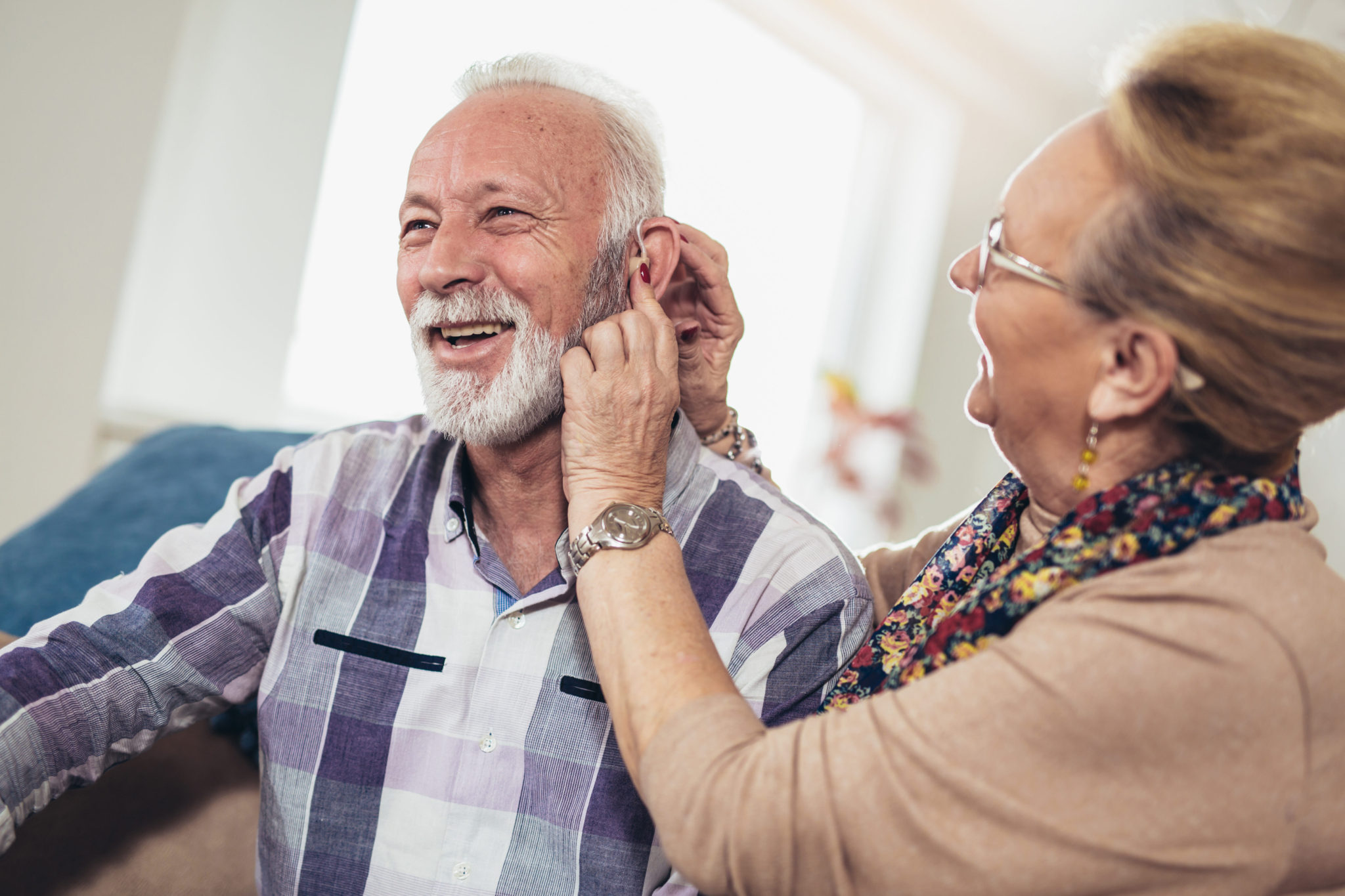 Older woman putting hearing aid in mans ear