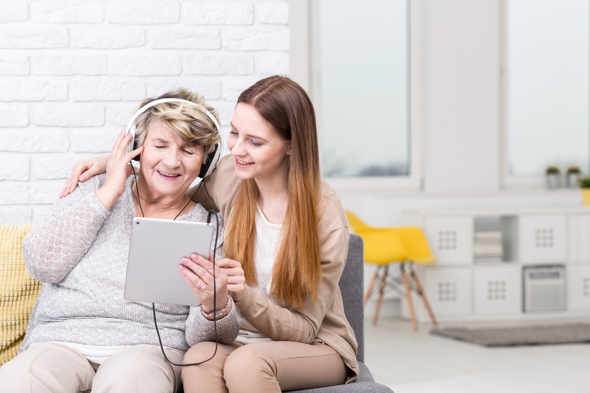 senior woman listening to music with her granddaughter sitting next to her