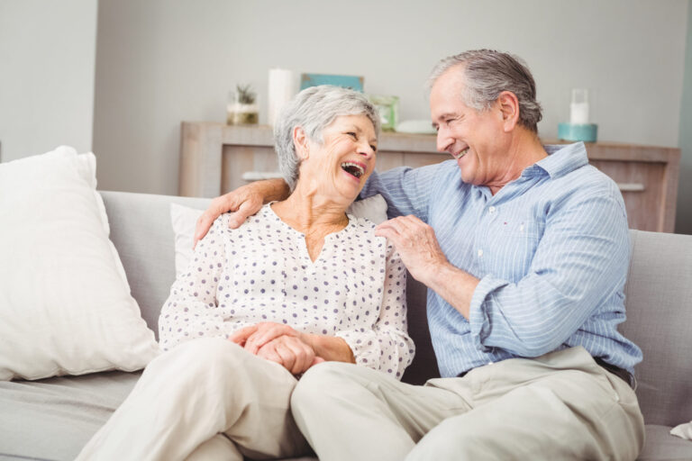 Romantic senior couple laughing while sitting on sofa at home