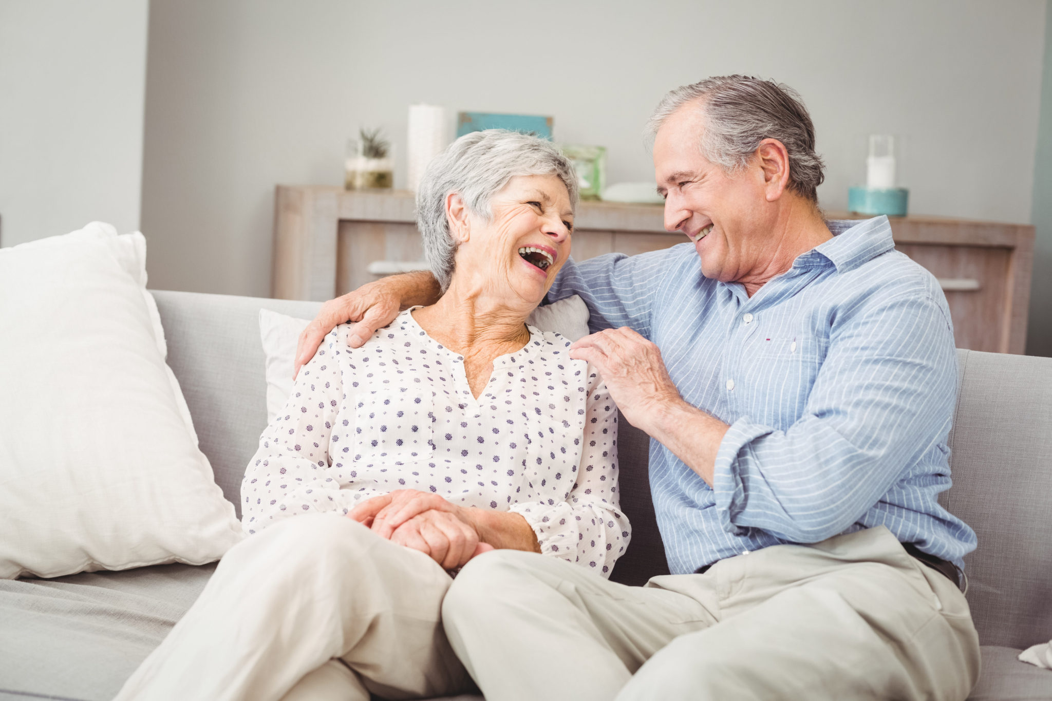 Romantic senior couple laughing while sitting on sofa at home