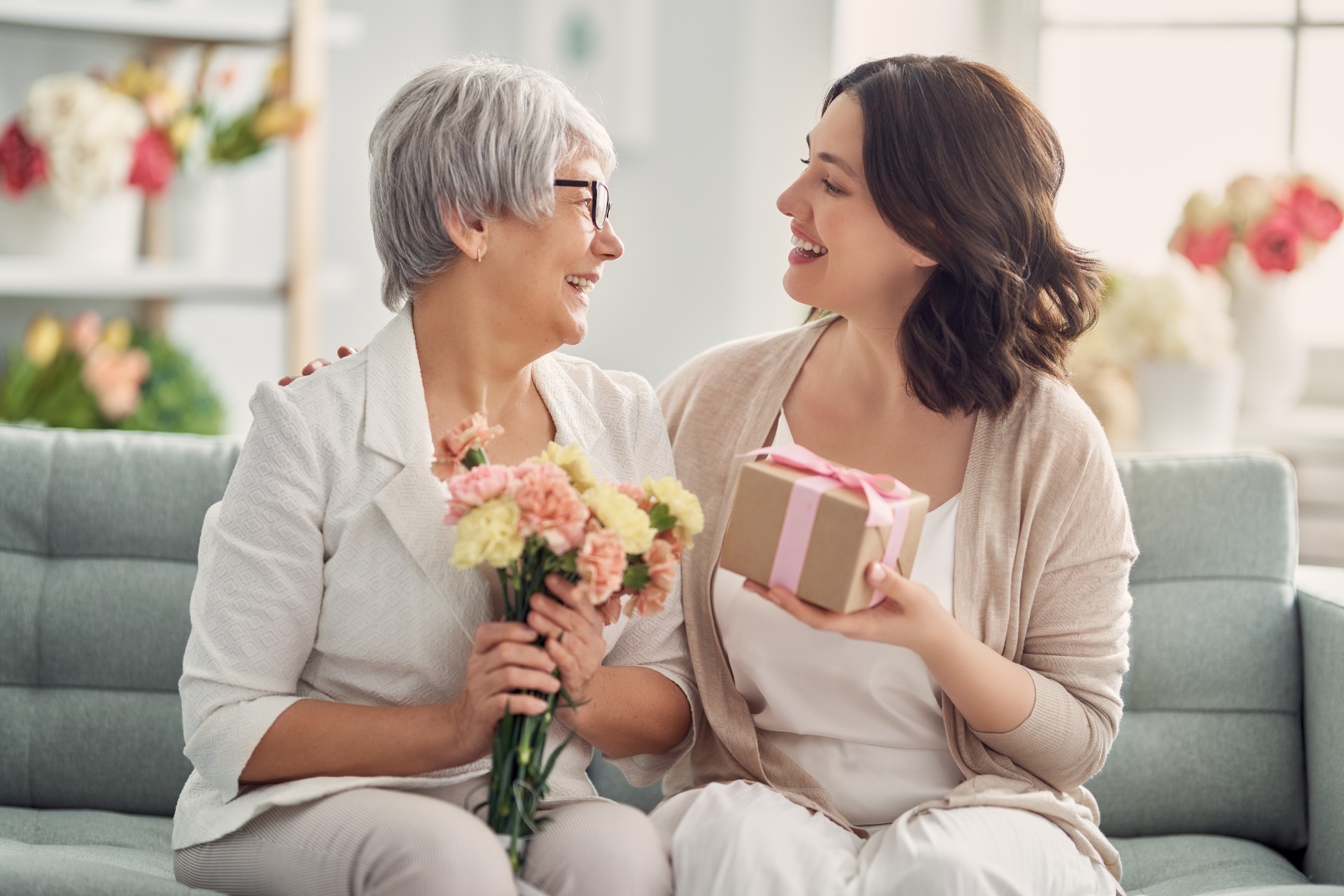 Senior mother and her daughter sitting on a couch exchanging gifts